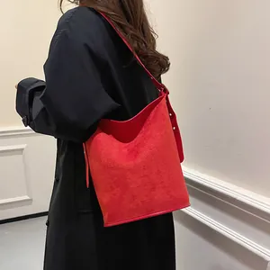 Detail of red suede bucket bag showing texture and wide strap on black coat
