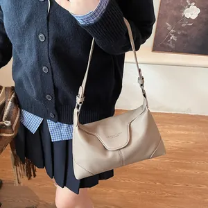 Détail d'un sac sous le bras beige à texture litchi avec logo embossé et boucle argentée