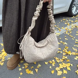 Detail of beige checkered quilted dumpling bag with ruffled shoulder strap in autumn setting