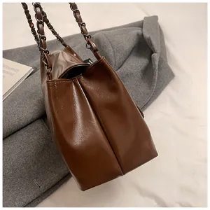 Detail view of deep brown faux leather tote with metal chain strap and side pleats