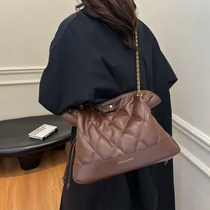 Detail of dark brown quilted chain bag with gold hardware on a model with black coat