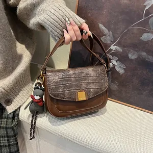 Detail der braunen Retro-Umhängetasche mit Kroko-Textur-Klappe und kleinem Bären-Anhänger