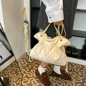Detailed macro view of quilted cream tote bag with gold chain straps and drawstrings