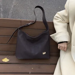 Close-up of a dark brown matte leather tote bag with a golden bean metal detail on wood
