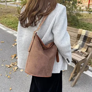 Close-up of deep brown suede bucket bag with adjustable leather strap in autumn setting