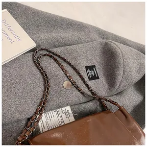 Detailed close-up of brown glossy leather shoulder bag with silver metal chain strap