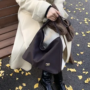 Close-up of a brown matte leather tote bag featuring a gold bean metal ornament