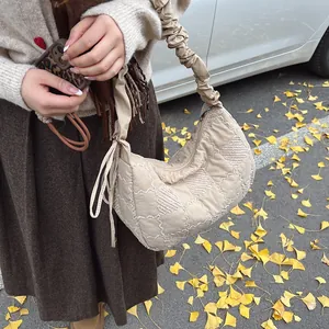 Detail of beige quilted dumpling bag with trendy ruched shoulder strap in autumn setting