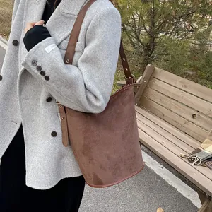 Detail of coffee brown suede bucket bag with metal rivet strap and reinforced base