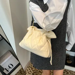 Close-up of cream quilted chain bag with gold hardware and drawstring detail on model