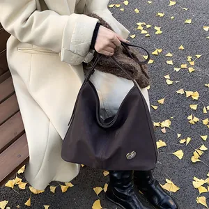 Detail of dark brown leather tote bag with silver heart logo on autumn leaf background