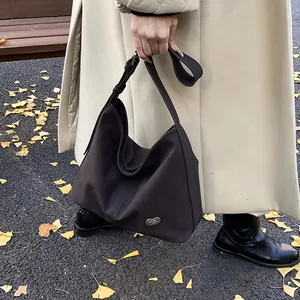 Detail of chocolate brown hobo bag with metal logo and wide strap in autumn setting