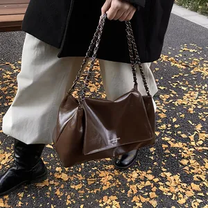 Detail of glossy dark brown tote bag with metal chain strap on autumn street
