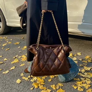 Close-up of dark coffee quilted leather tote bag with gold chain strap in autumn street setting