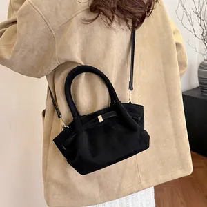 Detail of black suede tote bag with golden buckle hardware shown on shoulder