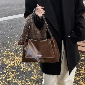 Detail of dark brown glossy leather tote bag with metal chain strap and white fashion text