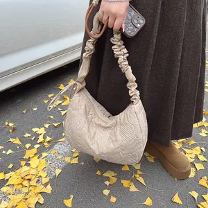Close-up of quilted beige dumpling bag with ruffled strap against autumn leaves