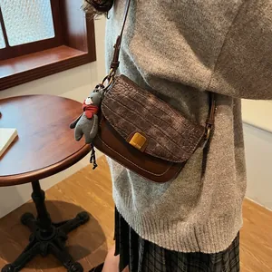 Details der braunen Umhängetasche im Vintage-Stil mit Krokoprägung und Bären-Anhänger
