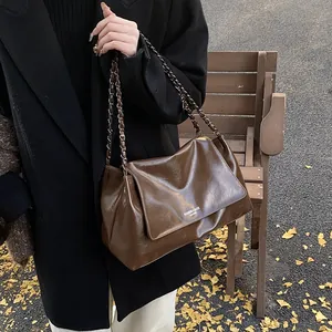 Detail of dark brown glossy leather tote bag with chain strap and elegant flap design