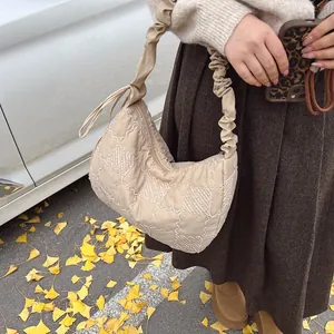Detailed view of beige quilted dumpling bag with ruched strap in autumn street setting