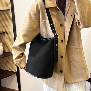 Detail of black suede bucket bag featuring wide shoulder strap with golden metal buckle