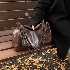 Close-up of deep brown tote bag with metal chain on park bench with autumn leaves