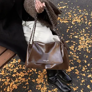 Close-up of brown glossy leather tote bag with woven chain strap on autumn street