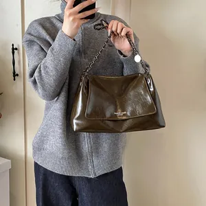 Detail of glossy dark brown leather tote bag with silver metal chain and circular charm