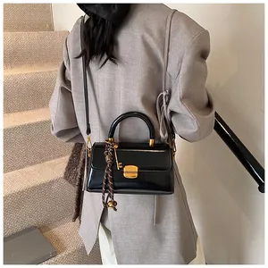 Detailansicht der Vintage-Wachsleder-Handtasche mit goldener Hardware auf grauem Blazer