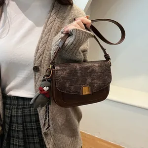 Details der braunen Tasche mit Krokoprägung, Goldschnalle und Plüschbär-Anhänger