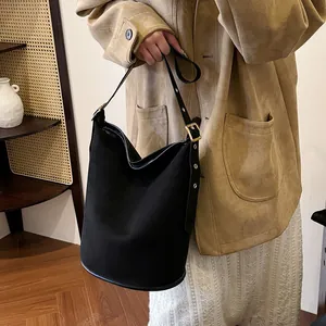 Close-up of black matte suede bucket bag featuring adjustable gold buckle on leather strap