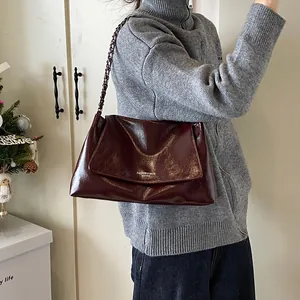 Close-up of stylish burgundy leather tote bag with chain strap worn by a model