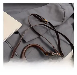 Detail einer dunkelbraunen Ledertasche mit Tragegriff und dekorativem Knotenanhänger