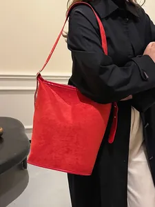 Red frosted suede bucket bag with adjustable strap worn over a black winter coat