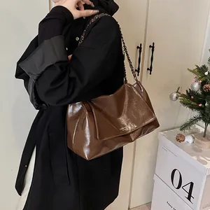 Detail of vintage brown patent leather shoulder bag with metallic chain strap worn by a model