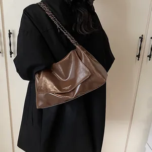 Detail of a dark brown oil wax leather shoulder bag with a metal chain strap on a black coat