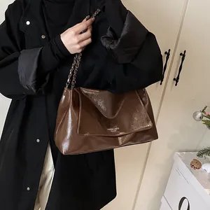 Detail of dark brown leather tote bag with glossy finish and metal chain strap
