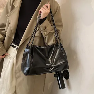 Detail of black glossy leather tote bag with elegant metal chain strap and sleek texture