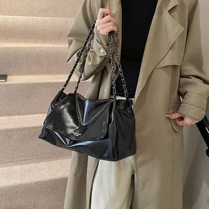 Close-up of black glossy leather tote bag with chain strap styled with a trench coat