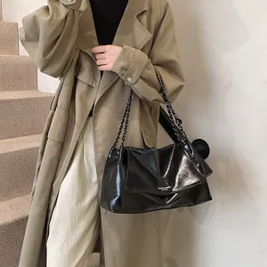 Detail of black glossy chain bag with leather folds on a khaki trench coat