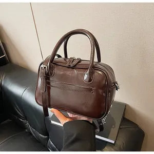 Detail of hand holding dark brown leather handbag with glossy finish and top zip closure