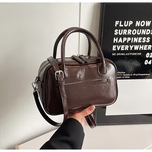 Detail of dark brown polished PU leather bag with double handles and adjustable strap