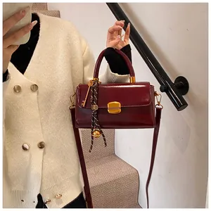 Detail der weinroten Lederhandtasche mit goldenem Schloss und gewebtem Seil-Accessoire