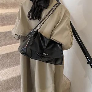Detail of glossy black leather tote bag with silver chain strap and white fashion text