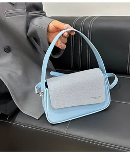 Détail d'un sac à main en cuir bleu clair avec rabat gris texturé et typographie mode