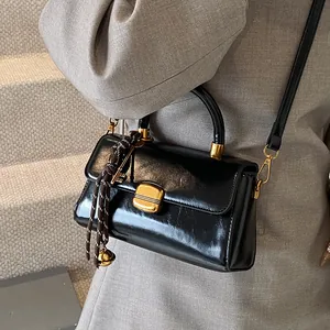 Schwarze Retro-Handtasche aus Ölleder mit goldenem Verschluss am grauen Blazer-Outfit