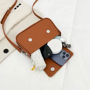 Sac bandoulière rectangulaire marron avec rabat ouvert montrant parapluie et téléphone