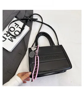 Detail of black glossy leather tote with logo embossing and a tennis racket charm