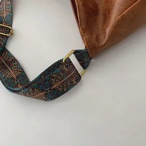 Detail einer braunen Leder-Eimertasche mit buntem Vintage-Gurt und goldener Metallschnalle
