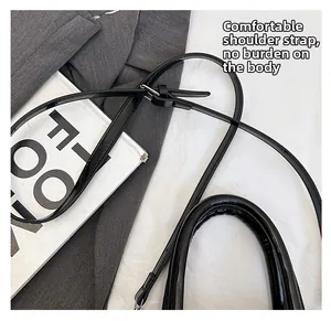 Detail of glossy black patent leather adjustable strap and silver metal buckle on tote bag